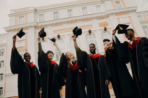 Graduates throwing their caps in front of a university building, open in the gallery viewer