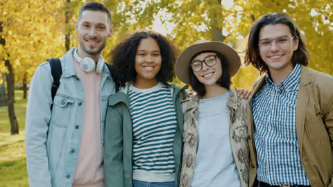 Four friends smiling together in a park in autumn